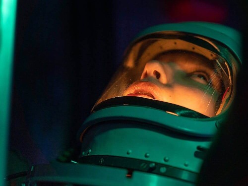 woman astronaut looking upwards, bathed in green light