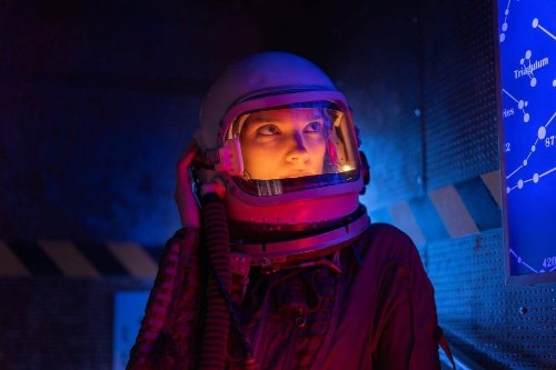 woman astronaut with helmet on. Her eyes are looking up to the top right